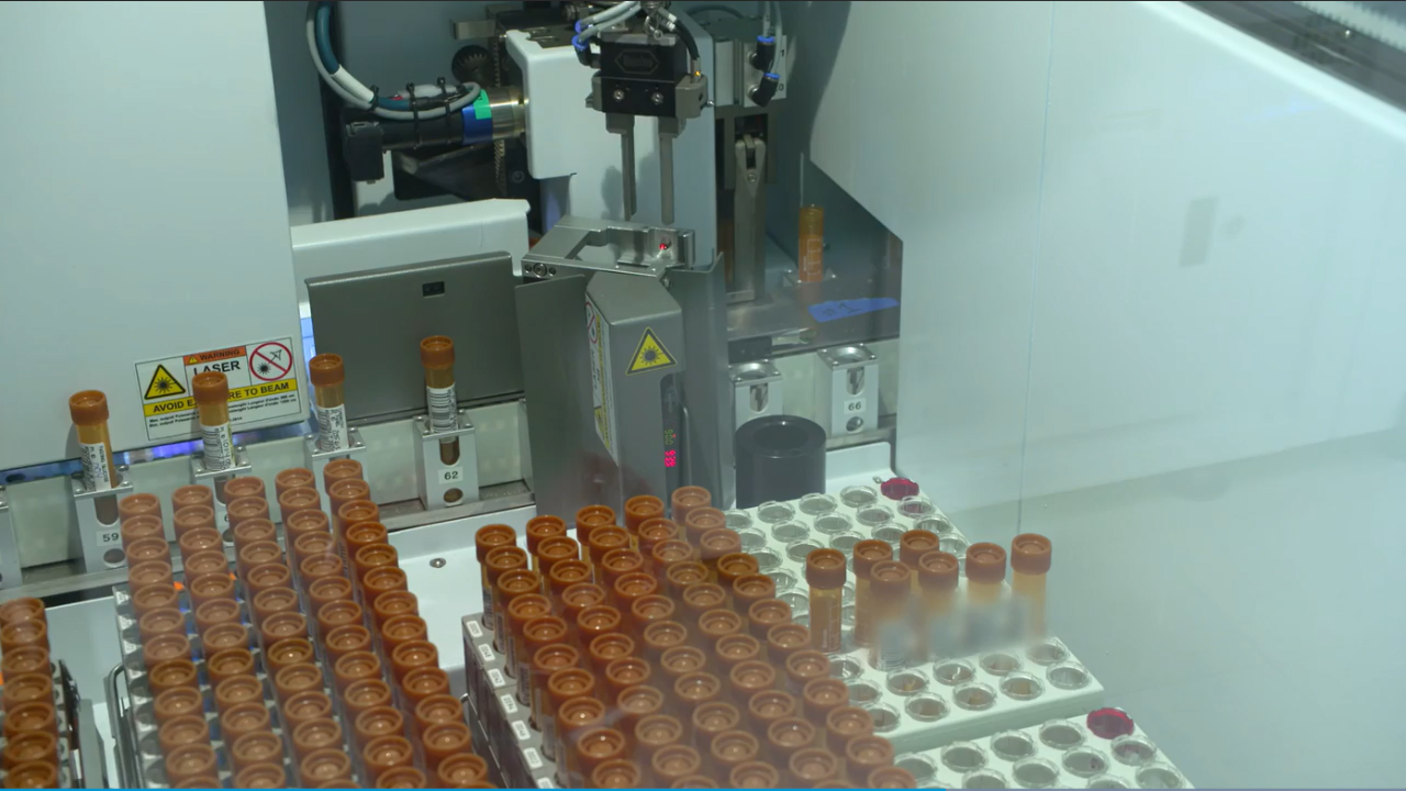 Image of test tubes inside of a clinical lab with a robotic arm in the background
